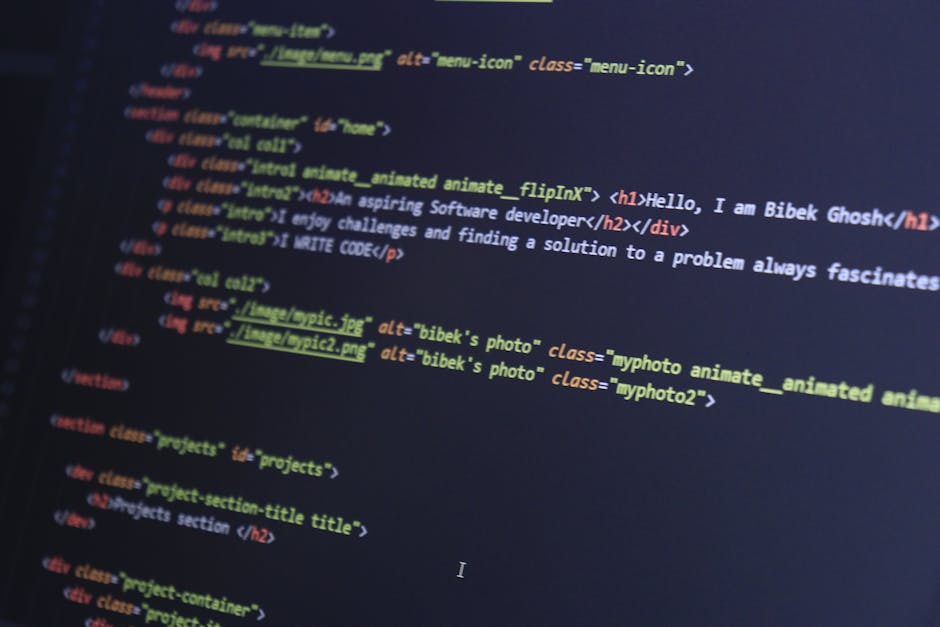 A person using a laptop computer with a dark-themed code editor open on the screen, displaying lines of colorful programming code. The laptop is placed on a dark, reflective surface, and the person's